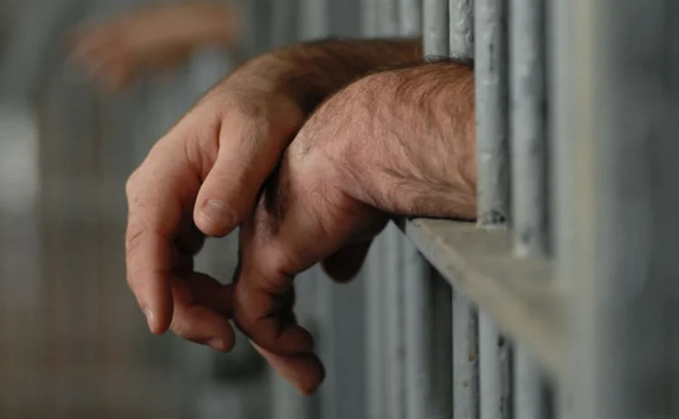 A man's hands sticking through prison bars