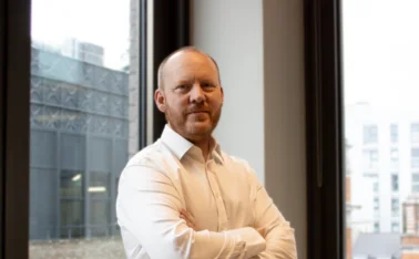 Dan McNally by a window with his arms crossed.