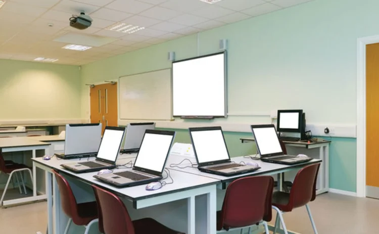 An empty classroom with a white board and a number of laptops