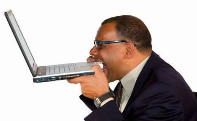 Businessman biting laptop in frustration