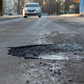 A pothole in the road and a car in the background that is moving towards this pothole